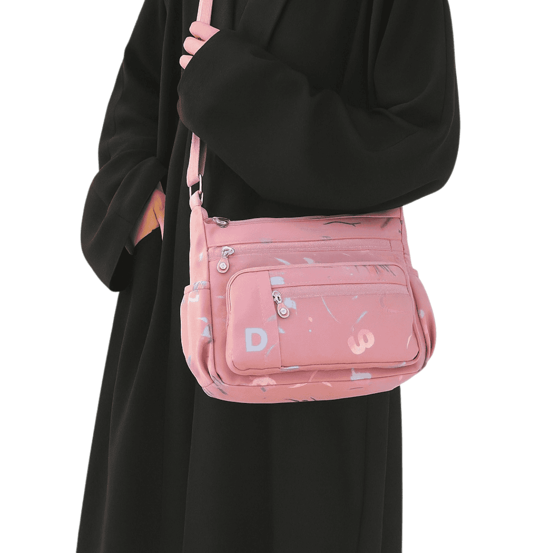 Pink crossbody bag with letter patterns worn by a women in a black abaya
